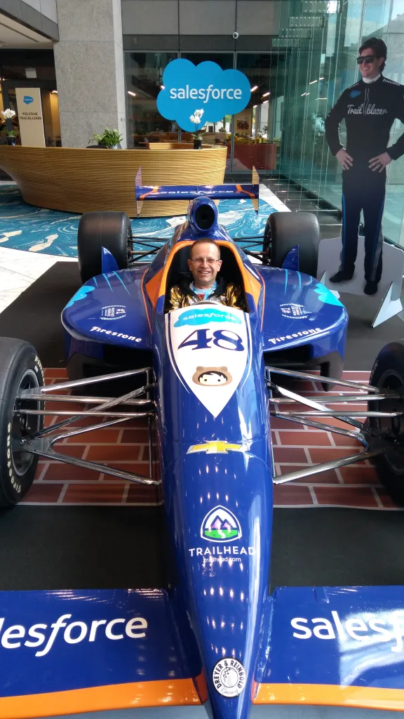 Paul sitting in a full racing car, within Salesforce's offices